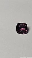 Close-up photo of the natural cushion cut raspberry spinel gemstone showcasing its pink-purple color and clarity.