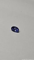 Oval cut purple-blue tanzanite gemstone lying flat, showing faceted top.