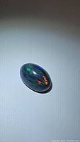 Oval black opal cabochon with multi-colored flashes under light showing green, red, blue, and orange hues.