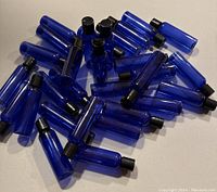 Top-down view of 32 cobalt blue PET refillable bottles with black press disc tops, scattered.