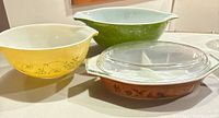 Four Pyrex bowls and casseroles arranged showing colors and design patterns including yellow floral, green, and brown woodland