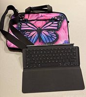 Butterfly printed pink carry case with black adjustable strap and removable black keyboard, showing front and top handles.