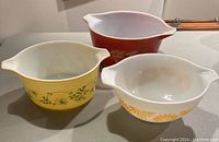 Three Pyrex Cinderella mixing bowls showing top and side views with various vintage patterns in yellow, white, and red colors.