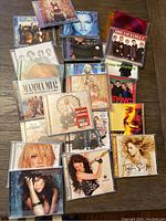 Top view of music CDs and empty cases spread out, showing artists including Britney Spears, JoJo, Ashlee Simpson, and soundtracks like Mamma Mia.