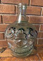 Front view of the large green recycled glass jug showing embossed wine-themed designs and text