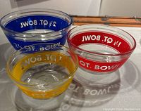 Set of three clear glass Anchor Hocking nesting mixing bowls with color bands in yellow, red, and blue, labeled with volume sizes; photo taken from top angle showing nesting and bright color bands.