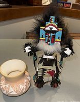Photo showing the full Navajo jug and Kachina doll side by side, highlighting the pottery's geometric designs and the Kachina doll's colorful mask and feather details.