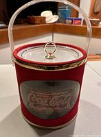 Front view showing red velveteen body, clear lucite handle, metal top rim, and lid with ring pull