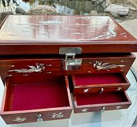 Opened jewelry box showing three drawers with red velvet lined interiors and mother of pearl accents on fronts.