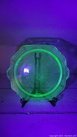 Uranium glass cake plate glowing bright green under UV light, showing the glass material's unique properties.