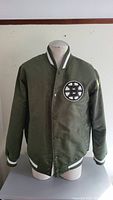 Front view of the Boston Bruins olive green jacket displayed on a mannequin showing the Boston Bruins logo patch on the chest with button snap closure.