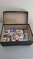 Box of sports cards showing a variety of players and sports inside a black box.