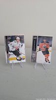 Two Connor McDavid hockey cards displayed on clear stands against a wall, one in white Oilers jersey and one in orange Oilers jersey.