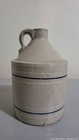 Front view of the crock jug showing the narrow neck and handle with blue pinstripes on beige stoneware.