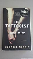 Front cover of the hardcover book 'The Tattooist of Auschwitz' showing the arm with a tattoo and the title text.