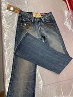 Full view of folded blue denim jeans showing vintage wash and studded pocket detail.