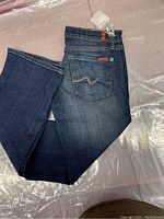 Folded dark blue denim jeans showing Swarovski crystal embellishments on back pocket and brand leather patch on waistband.
