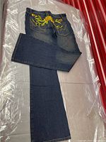 Full length photo of dark blue denim jeans folded showing embroidery on back pockets and leg