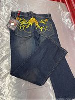 Blue denim jeans folded showing the back pockets and leg with yellow floral embroidery.