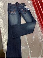 Full view of dark blue denim jeans with flare leg styling and visible embroidered back pockets