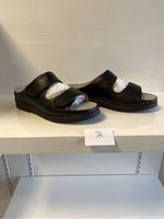 Side view of a pair of black ladies slip-on shoes with adjustable straps, showing left and right shoes.