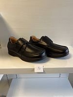 Side and angled view of the pair of men's black leather shoes size 43 extra wide. Shoes have a wide strap and rounded toe with detailed stitching.