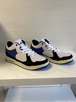 Side profile view of the men's athletic sneakers showing the white, black and blue color patterns, perforated side panel and number '44' on the tongue.