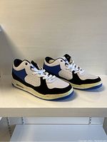 Side view of a pair of men's Air sneakers in white, blue, and black on white shelf.