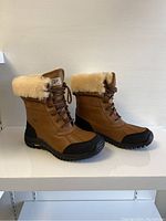 Side view of both boots showing leather upper, shearling collar and rubber lower shell