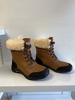 Three-quarter view of both boots showing leather upper, sheepskin cuff and lace-up front