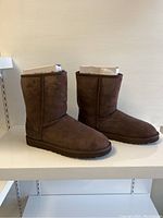 Left side angle view of brown UGG classic short boots in original packaging, showing suede material and shape.