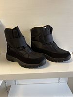 Side angle view of black winter boots showing shape, strap detail and sole thickness.