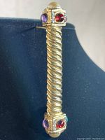 Gold tone bar pin with twisted design and multiple colored cabochon stones on each end photographed from front angle.