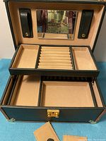 Open jewelry box showing interior with compartments, ring slots, two black leather necklace straps, and an interior mirror.