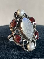 Close up front view showing marquise moonstone, garnet stones, and pearls in sterling silver setting.