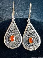 Front view of teardrop sterling silver earrings with orange center stones placed on black background.
