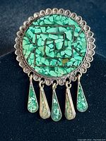 Front view of circular sterling silver brooch pendant featuring green malachite stone inlay spiral pattern and dangling five teardrop malachite drops.