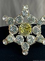 Close-up front view of vintage star-shaped brooch showing clear rhinestones and central yellow rhinestone in silver-tone metal setting.
