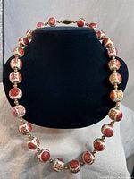 Full view of vintage Asian beaded necklace displayed on a black bust stand showing large cream and red hand painted beads with metal spacers.