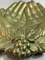 Close-up photo of the top of the brass clasping hands dish showing detailed grapes and leaves in the center with the hands forming the base.