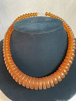 Front view of vintage amber-orange plastic beaded choker necklace on display bust showing bead shape, size, and color.