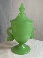 Front view of the jadeite glass covered cup with koi dolphin shaped handles and pointed lid with spiked knob