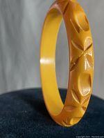 Close up photo showing hand carved floral or leaf motifs on the light brown Bakelite bracelet.