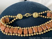 Close-up view of the lobster claw clasp, ornate textured round metal bead connectors, and rectangular goldstone beads along with small round metal beads.