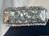 Close-up of rectangular granite stone set in ornate sterling silver frame showing speckled granite pattern with black, white, and gray tones.