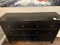 Front view of the black brown IKEA dresser showing all 8 drawers and metal knobs.