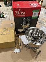 Original All-Clad branded box, ceramic insert box, stainless steel fondue pot with lid and stand showing the entire setup.