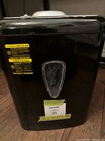 Front view of the black Amazon Basics shredder showing warning label and MaxSold tag with measurements on bottom.