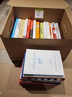 Photo showing the entire lot of leadership and business books packed in a cardboard box and stacked with a few books on top.