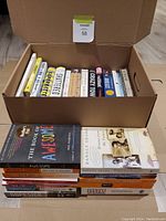 Box filled with multiple paperback and hardcover non-fiction and biography books including titles focusing on social issues and political biographies.
